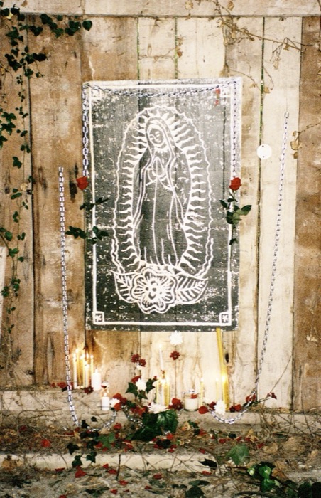 Full view of the Mother Mary altar piece lit by candles among ivy and roses